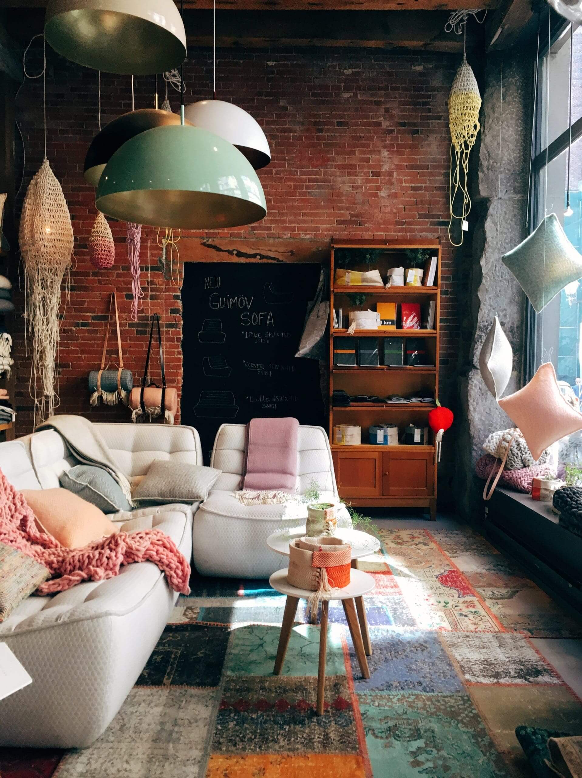 A living room having a brick wall, glass windows and containing a white sofa with throw pillows